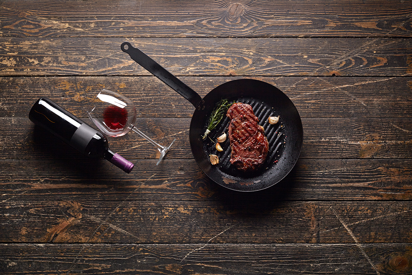 Marbled beef steak in a grill pan with a bottle of wine and wine